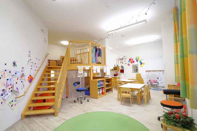 Igelgruppenraum mit Treppe zur empore, Sitzgruppen und Kinderzeichnungen an der Wand