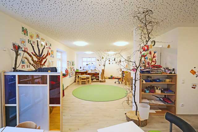 Blick in die Baumgruppe, im Vordergrund Bücherregale als Raumteiler, im Raum stehen natürliche Äste in Baumscheiben befestigt
