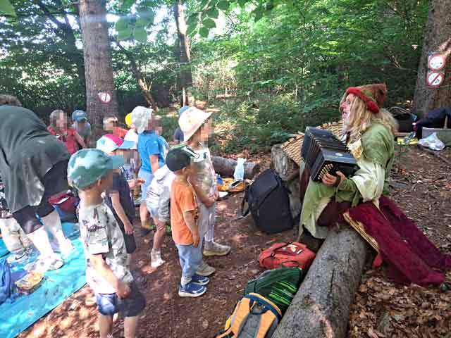 Eine Gruppe Kinder lasucht im Wald der Pimpernella Pumpelsack beim Spiel mit dem Bandoneon.