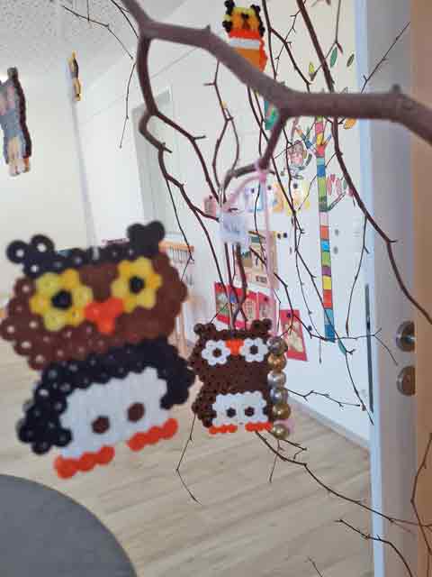 Zwei Eulen aus Bügelperlen hängen an einen Ast im Gruppenraum