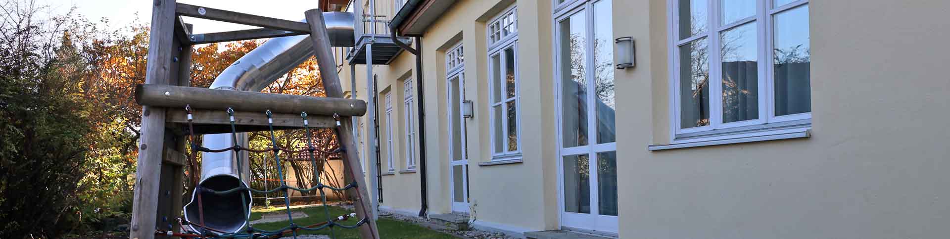Rutsche aus Obergeschos an der Hausfassade, davor Klettergerüst